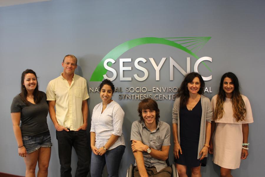 A photo of the Fishing & Urban Inequality team gathered in front of the SESYNC logo