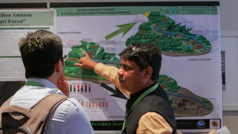 A man pointing to a scientific poster, explaining a concept to another man. 