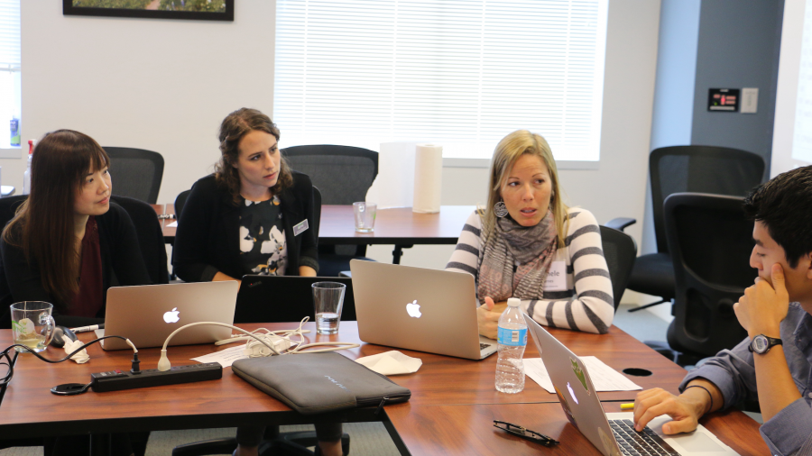 A group of four researchers gathered around a table with laptops engaged in a discussion