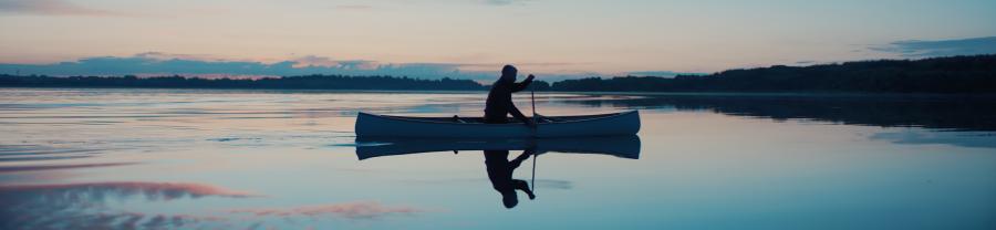 A photo of a person paddling in a canoe on a lake in silhouette