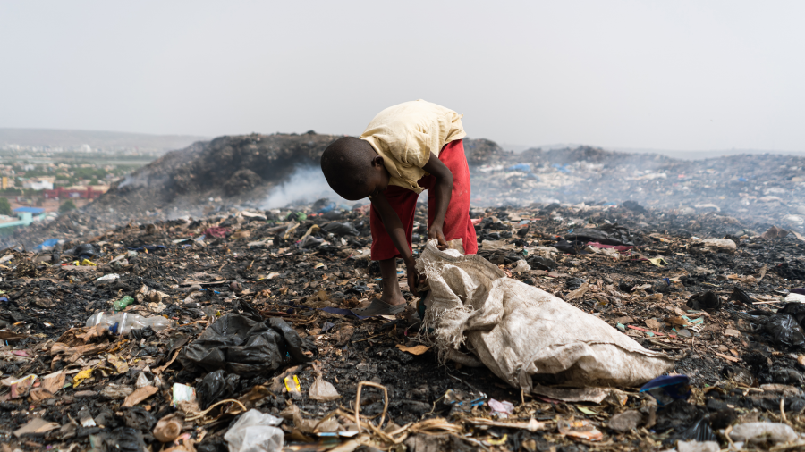 A young boy scooping garbage into a bag while standing in a dump