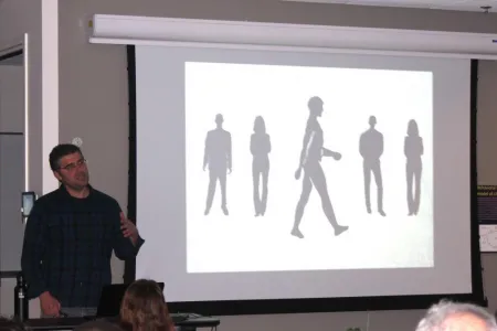 Gregory Bratman presenting in front of an image of screen with an image of five human figures