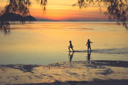 The silhouettes of two children playing in water with a sunset in the background
