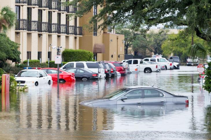 "Cars submerged in water in a flooded parking lot next to an apartment building.